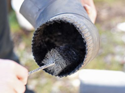 man sweeping out section of chimney pipe with small brush